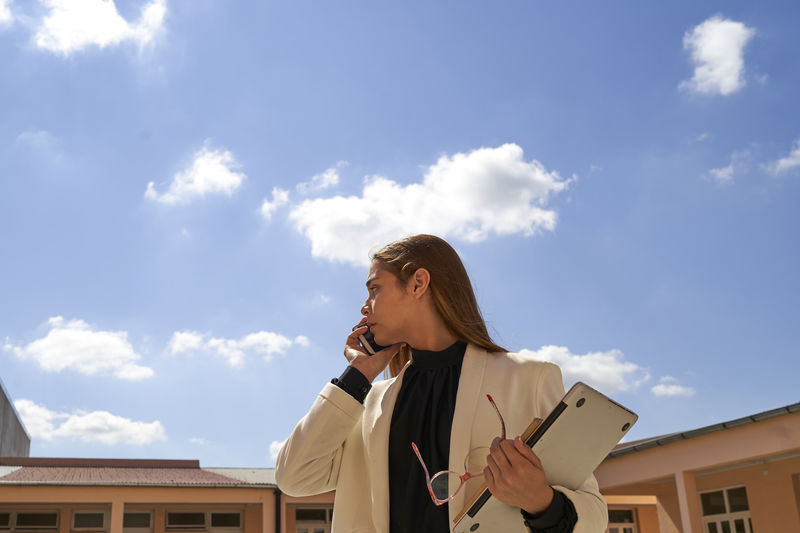 Confident beautiful business lady talking on the phone, with the blue sky as background. 