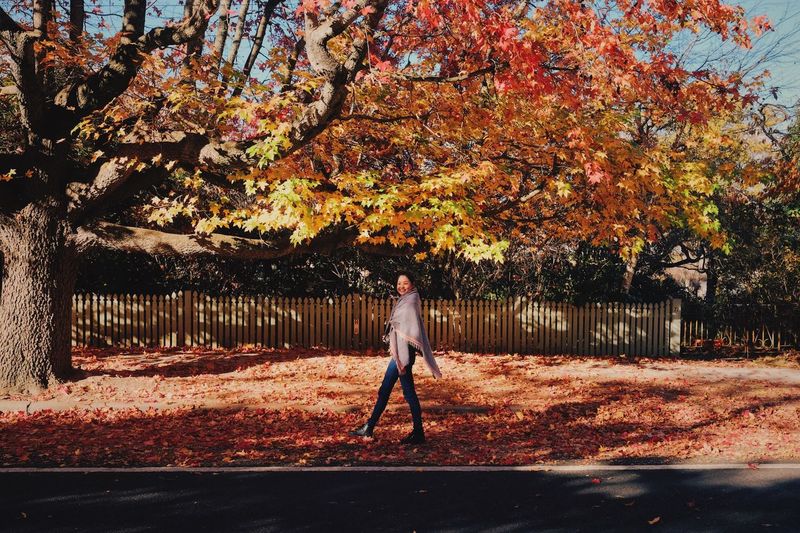 Side view of woman walking on sidewalk during autumn