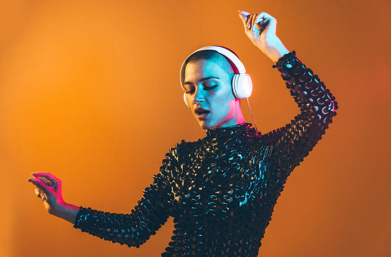 Young woman with shaved head wearing headphones against orange background