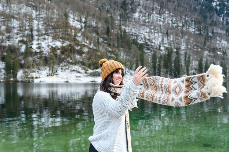 Young woman in winter sweater smiling, standing by a lake.