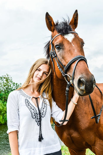 Portrait of woman standing with horse against sky