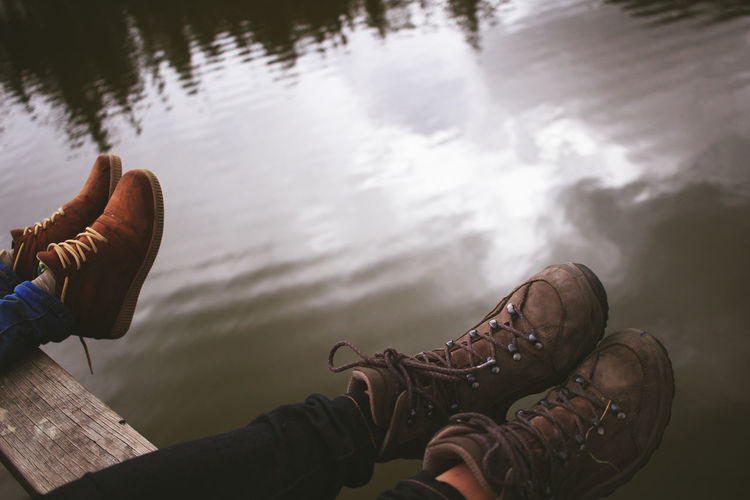 Low section of people wearing shoes while sitting on pier over lake