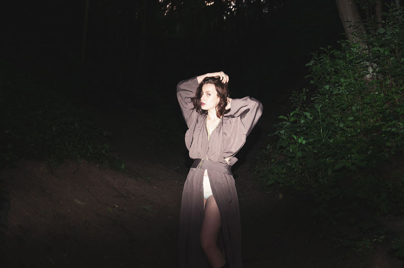 Portrait of young woman standing in forest at night