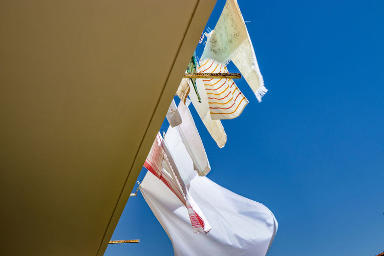 Low angle view of clothes hanging against clear blue sky