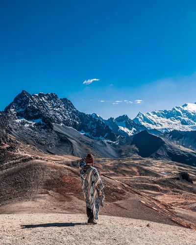 Rear view of woman standing on mountains against blue sky