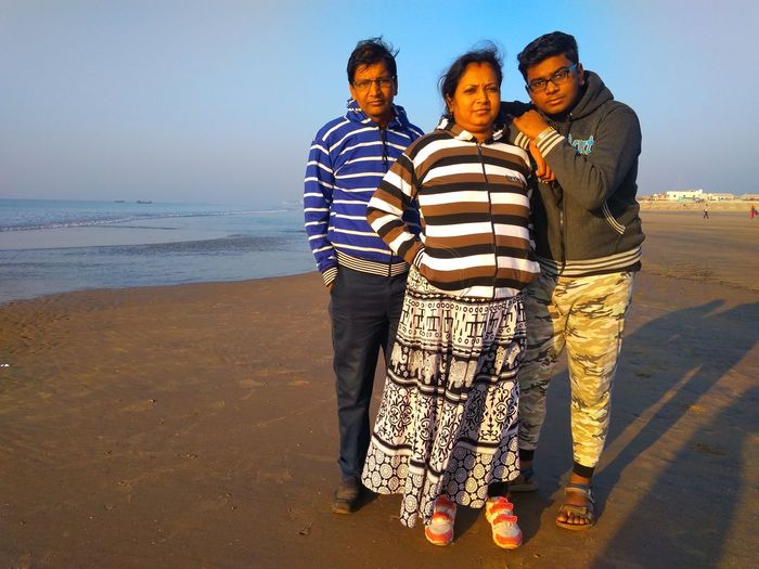 Portrait of family standing at beach against clear sky during sunset