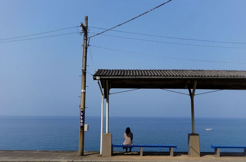Rear view of woman sitting on bench against sea and sky