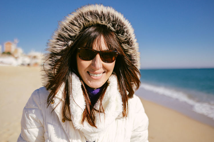 Happy woman in white jacket and sunglasses on a sunny winter day at the beach