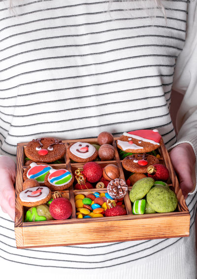 Gingerbread cookies with colorful icing, mint cookies, sweets, nuts and ornaments in woman hands