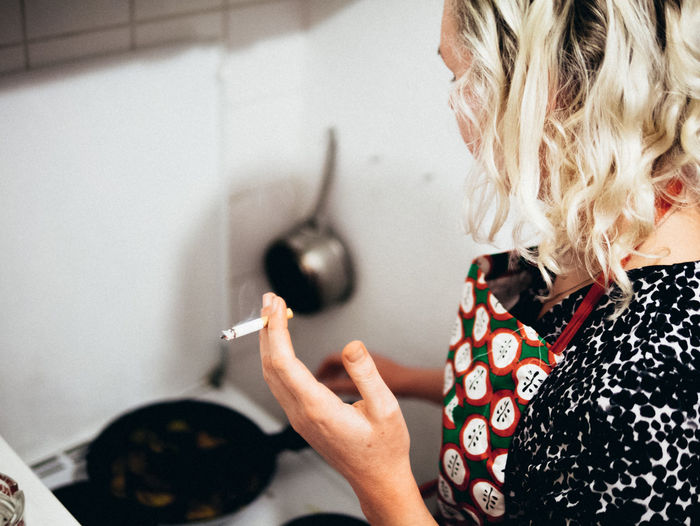 High angle view of woman smoking cigarette while cooking in kitchen