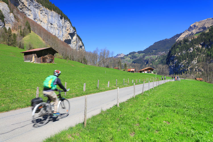 Rear view of person cycling on road amidst field against clear sky