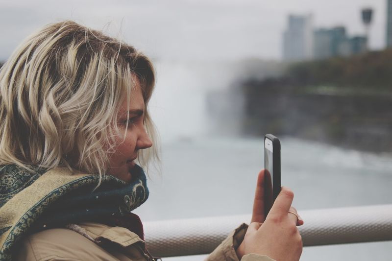 Close-up of woman using mobile phone while standing by railing in city