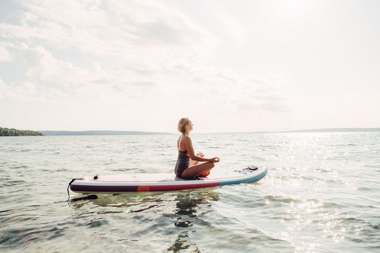 Full length of woman mediating on surfboard in sea