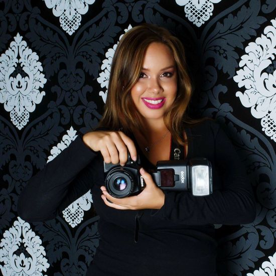Portrait of smiling young woman holding camera at home