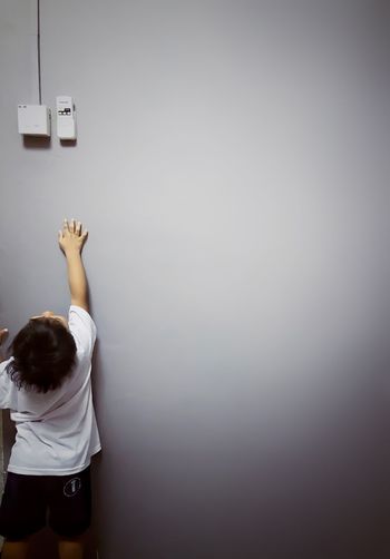 Rear view of boy reaching towards fuse box over gray background