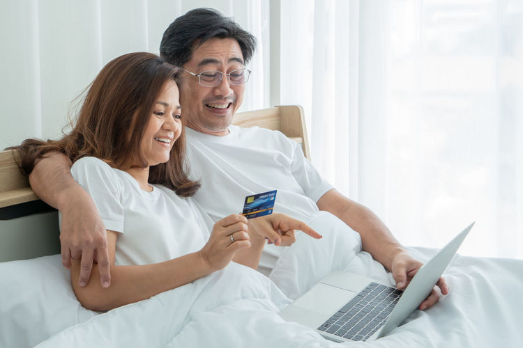 Happy couple shopping through laptop in bedroom