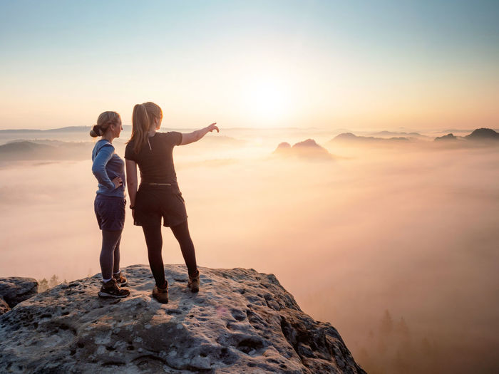 Fearless girls on rocky edge. hiker shows girl friend something interesting in far misty distance