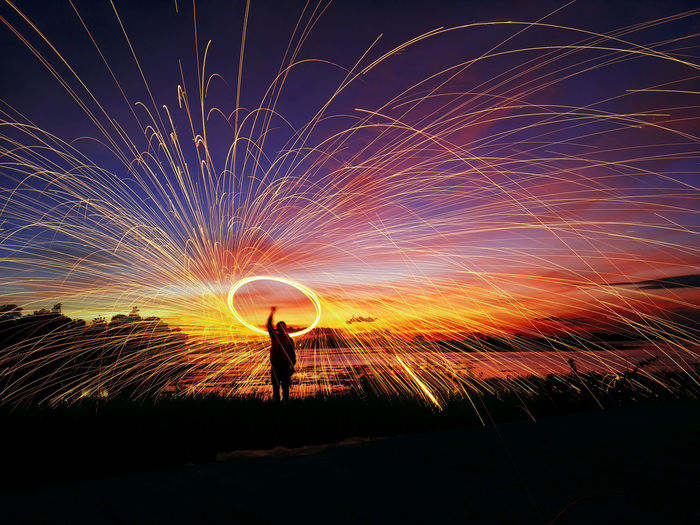 Silhouette man spinning wire wool at beach against sky during sunset