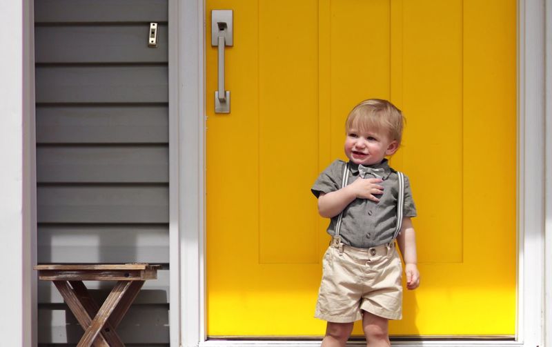 Portrait of a small boy standing in front of a yellow door