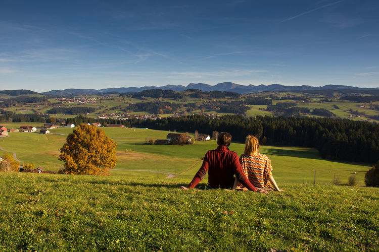 Rear view of couple sitting on field against sky