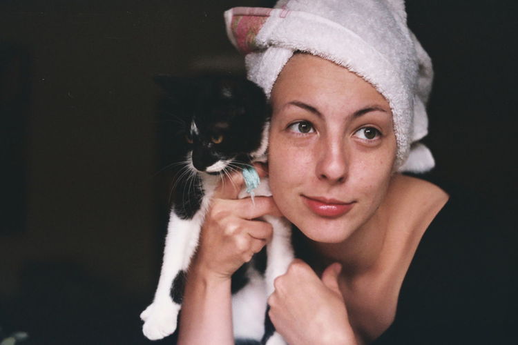 Portrait of beautiful young woman holding cat against black background