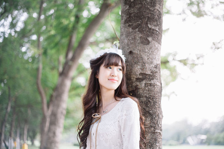 Woman looking away against tree trunk