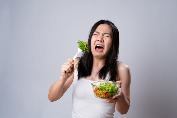 Young woman eating food against white background