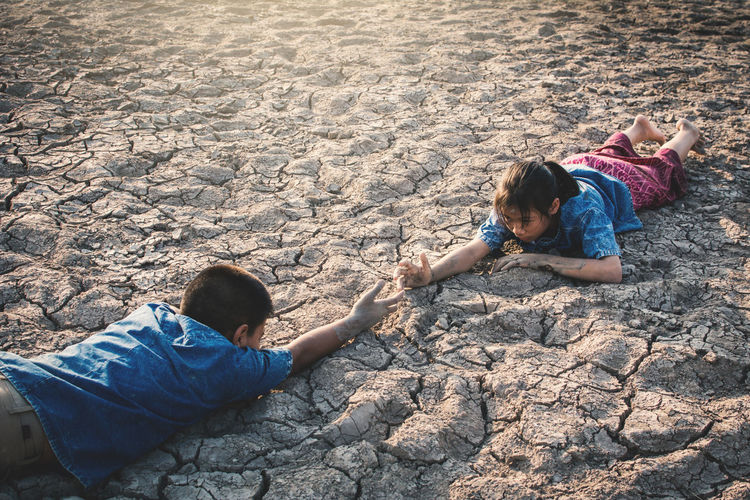 High angle view of siblings lying on barren landscape