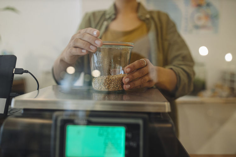 Midsection of female owner weighing grain jar on weight scale in cafe
