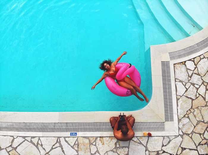 High angle view of woman swimming in pool while man sitting on poolside