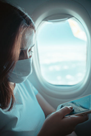 Peaceful girl on the airplane with medical mask and doing like sign and looking at the camera.