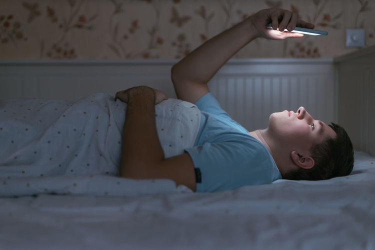 Young woman using mobile phone while lying on bed at home