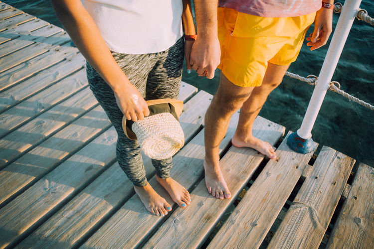 Low section of couple standing on boardwalk while holding hands