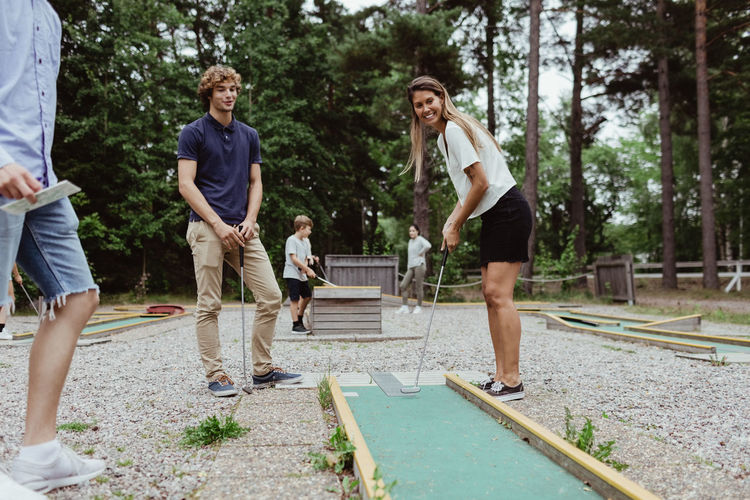 Full length of smiling friends playing miniature golf in backyard during vacation