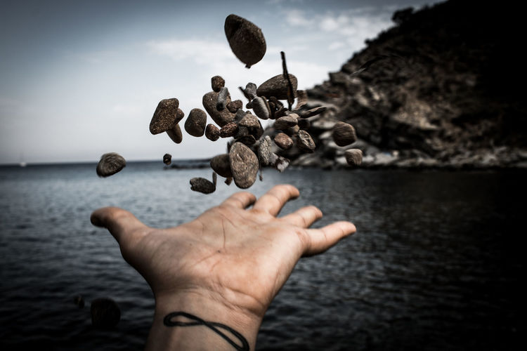 Cropped hand throwing rocks over sea