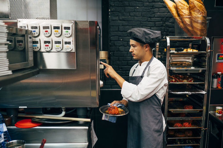 Side view of man putting timer on metal appliance while working in restaurant kitchen