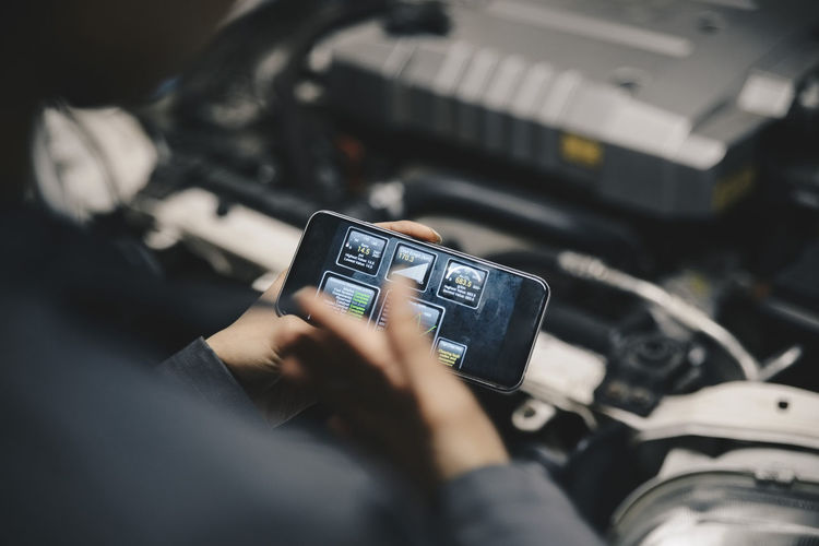 Cropped image of mechanic using application on smart phone by open car