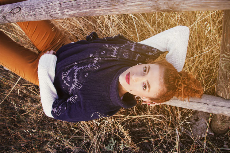 Portrait of young woman lying on railing at field