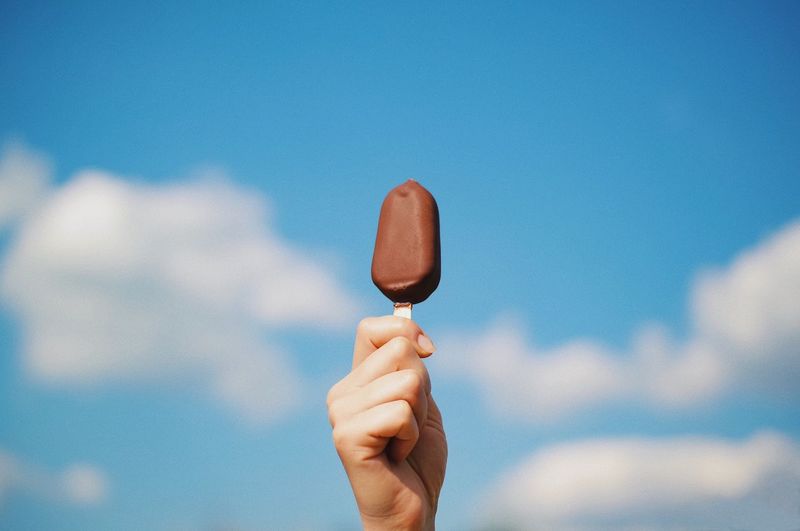 Close-up of hand holding ice cream against sky