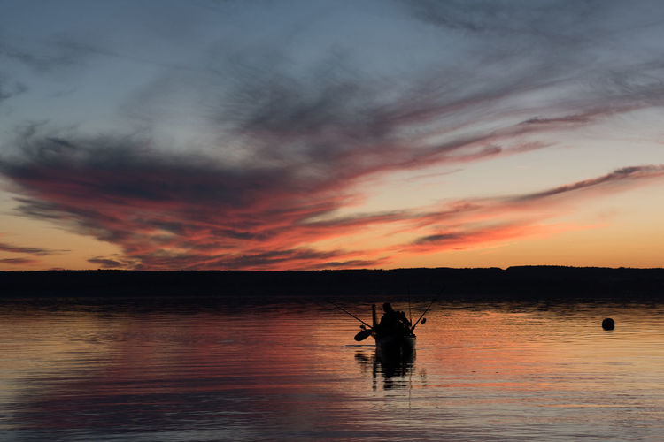 Silhouette men on boat against sky during sunset