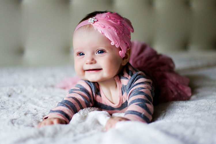 Baby girl lying on her stomach and smiles on the bed in clothes and a pink headband