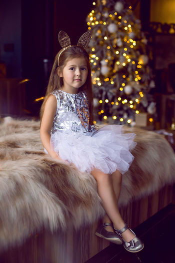 Girl in dress and with bunny ears sitting on bed with fur in studio dress in christmas