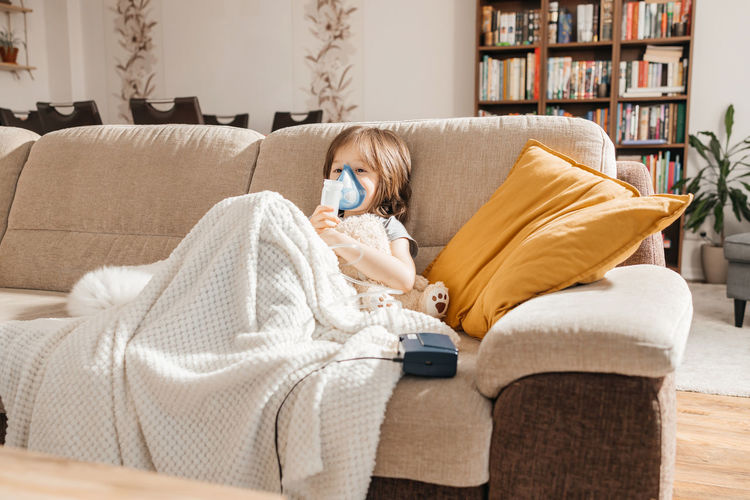 Little boy makes inhalation with a nebulizer at home lying on the couch. cough prevention 