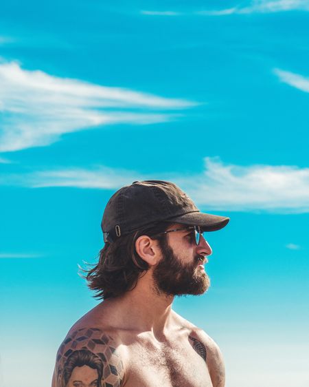 Shirtless man wearing cap against blue sky
