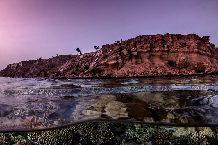 Scenic view of sea and rock formation against clear sky during sunset