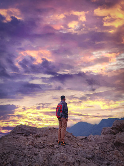Rear view of man standing on rock against sky during sunset