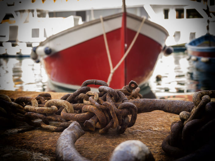 Close-up of rusty metallic chain against red boat at harbor