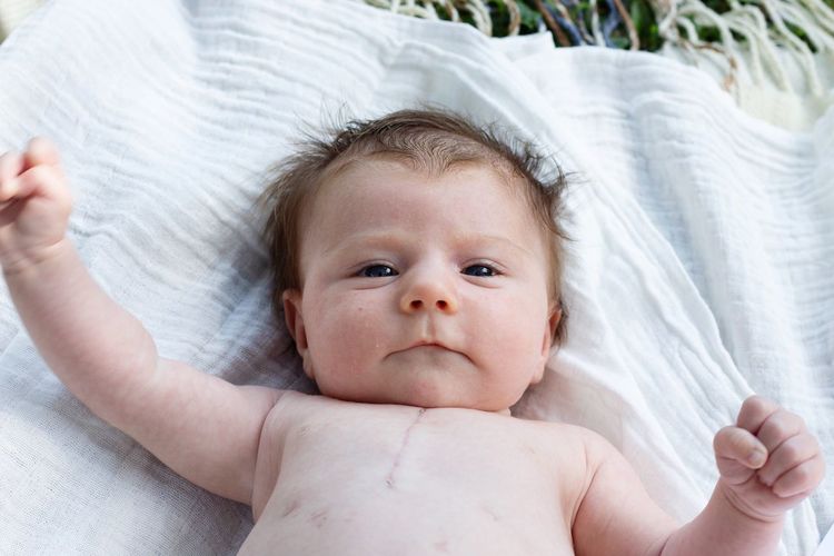 High angle portrait of cute shirtless baby girl lying on bed at home