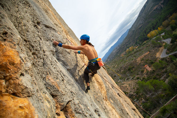 Shirtless man rock climbing against sky
