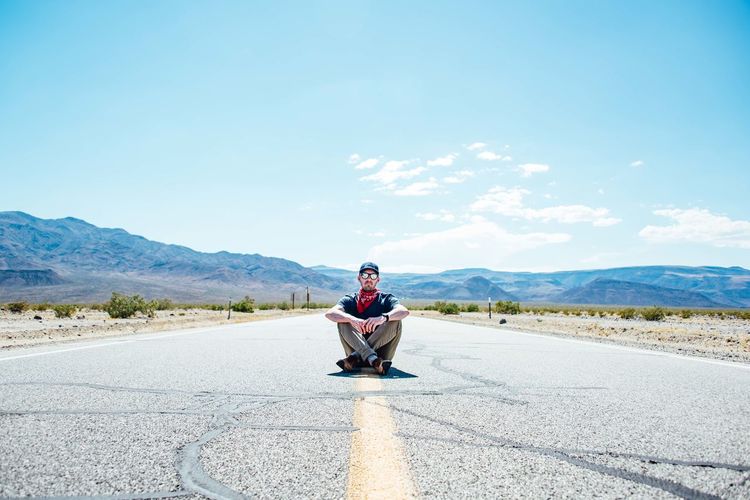 Man sitting on road against mountain range